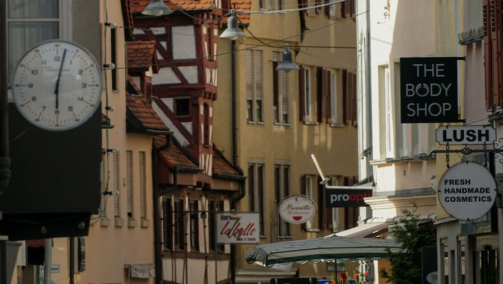 Натовп людей на вузькій пішохідній вулиці зі старовинними будинками та різноманітними вивісками магазинів в Ульмі.