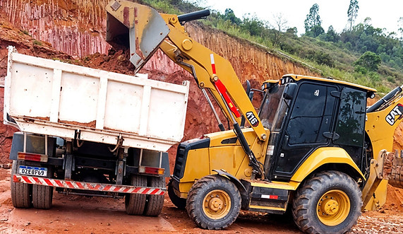 Escavadeira e caminhão basculante em serviço de terraplanagem.