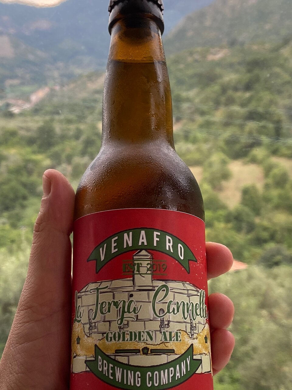 Una bottiglia di birra del Molise tenuta tra le mani con uno spettacolare sfondo sulle campagne del Molisane