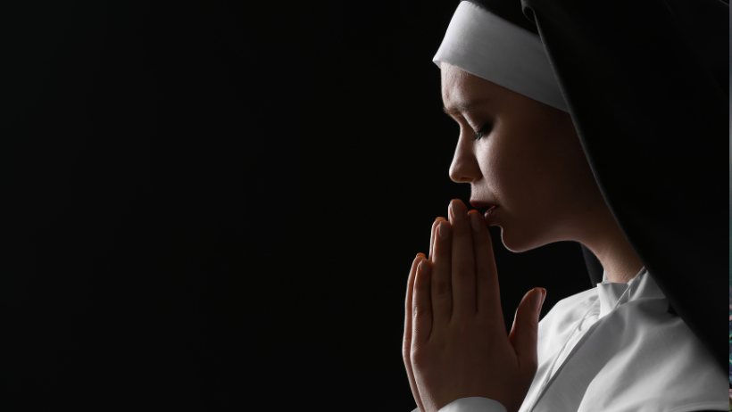Una suora molto pensierosa, mentre sta pregando in una stanza buia