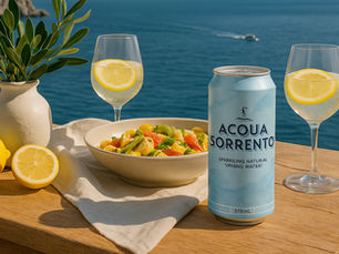Acqua Sorrento sparkling water can placed on soft beach sand under a striped coastal umbrella, with turquoise water and a bright summer sky in the background.