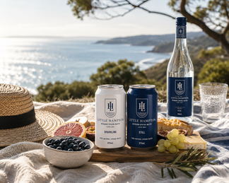 Little Hampton still and sparkling spring water cans and glass bottle displayed at a luxury Australian coastal picnic setting overlooking the ocean.