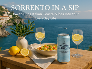 Acqua Sorrento sparkling water can on a coastal Italian-style table with lemons, pasta, wine glasses and an ocean cliff backdrop