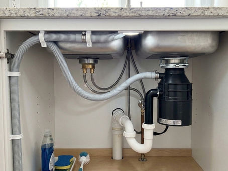 A correctly installed dishwasher drain hose featuring a secured high loop connected to a garbage disposal above the P-trap under a kitchen sink.