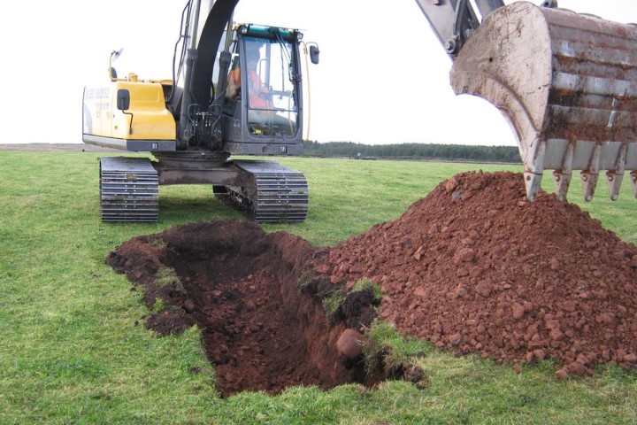 Excavated trench and soil spoil on grass
