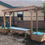 Thumbnail: 10' shade arbor with side storage units with lids over a water table at a school playground