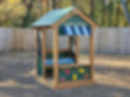 Green Playground playhouse with fruit images, a counter, shelves, a chalkboard, bins, a striped  awning, and a roof.