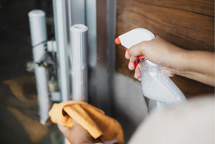Hands wiping down a glass surface with a yellow cloth in a Tucson home, with a spray bottle in use. The simple act of house cleaning takes place against a backdrop of wood and metal.