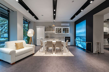 A bright Tucson condo kitchen and living space with sleek white cabinetry, soft beige seating, and dark flooring that contrasts the clean lines of the room. Floor-to-ceiling windows and a sculptural light fixture add a sense of openness and style to the carefully designed interior.