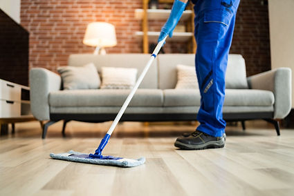 A person mops a wooden floor in a Tucson living room, with a grey couch, brick accent wall, and cleaning supplies nearby—capturing the care and effort behind professional home cleaning.