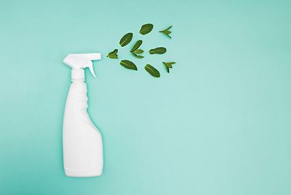 A stylized image of a white spray bottle on a turquoise background, with bright green leaves spraying from the nozzle instead of liquid. This Tucson-inspired visual highlights a fresh approach to green cleaning, symbolizing plant-based products and environmentally conscious care.