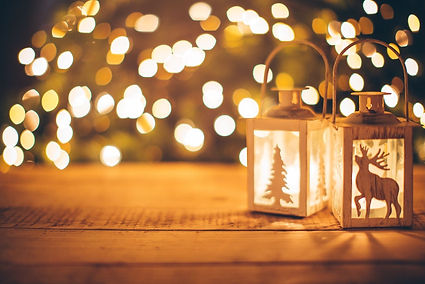 Two decorative lanterns sit atop a wooden surface in a Tucson home, glowing from within with festive silhouettes—a reindeer and a Christmas tree—cut into their sides. The blurred, warm background lights evoke the quiet charm of a holiday evening, where small touches bring seasonal spirit into the home.