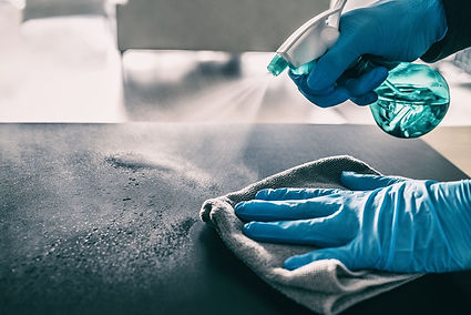 A person wearing blue gloves disinfects a bathroom counter in a Tucson home, spraying cleaning solution and wiping down a bright, polished surface. Brass fixtures and pendant lights frame the moment, highlighting attention to detail and the quiet impact of a freshly cleaned space.