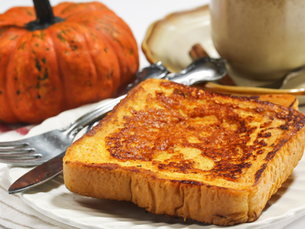 Golden-brown pumpkin spice French toast on a white plate with a small pumpkin and coffee cup in the background, a cozy fall breakfast idea.