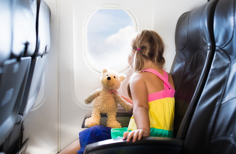 Toddler sitting in an airplane window seat with a stuffed animal while traveling