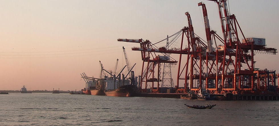 Port industriel au coucher du soleil, grands portiques rouges, navires et petite barque sur l’eau.