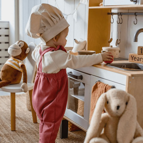 Child dressed as chef playing with kitchen set