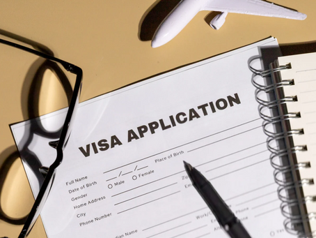 Visa application form on a desk with a pen, glasses, notebook, and a toy plane. Represents study abroad or immigration planning.