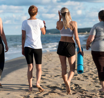 Four women walk on beach, yoga mat in hand