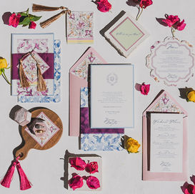 Mediterranean wedding invitation suite with floral details, scalloped menus, pink and blue envelope liners, tassels, and bougainvillea petals.