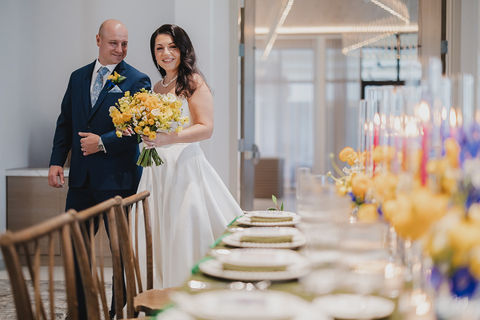 Bride and groom entering a wedding reception space with vibrant floral tablescape and candlelight in the foreground.