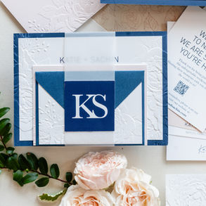 Flat-lay of Katie and Sachin’s elegant navy and white wedding invitation suite with embossed details and floral accents.