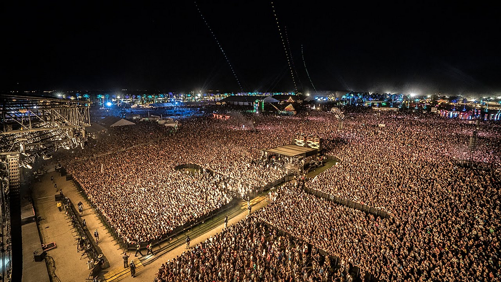 Large crowd gathered around a central stage during a nighttime festival performance.