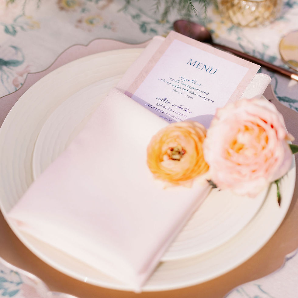 Elegant place setting with a white plate, pink napkin, and menu card. Accented by soft pink flowers, creating a romantic, festive mood.