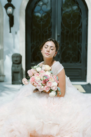 A portrait of quiet confidence, this Fairycore bride lets her dress and bouquet do the speaking. Cradled in layers of soft blush tulle and framed by romantic natural light, she holds a garden of curated roses—each bloom as tender as the vows to come. This image reminds us that elegance isn’t always loud. Sometimes, it’s felt in stillness.