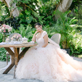Bathed in morning light, our bride savors a quiet tea amid the lush greens—her gown spilling like clouds at her feet. Every detail on this table tells a story of softness, sweetness, and anticipation. The celebration hasn’t started yet, but magic already lingers in the air.