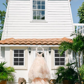 Framed by sunlight and tropical palms, this ethereal gown sets the tone for everything to follow. Its cloud-like layers of blush tulle echo the textures in the invitation suite and the palette of the shoot. More than a fashion moment, this dress is the heartbeat of the story—whimsical, romantic, and unapologetically bold. It reminds us that when style and emotion align, the celebration begins long before the walk down the aisle.