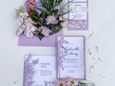 Lavender wedding invitation suite with layered cards, cut floral details, envelope, RSVP card, thank-you note, and fresh flowers