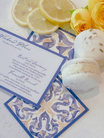 Flat lay of Mediterranean-inspired wedding itinerary card with lemons, roses, and macarons