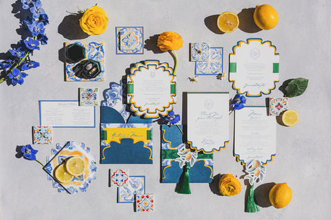 Flat lay of Amalfi Coast-inspired wedding invitations with lemons, blue tiles, and floral accents.