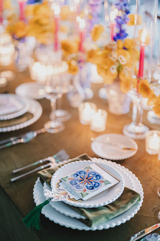 Close-up of Mediterranean-inspired place setting with ceramic tile, green napkin, and layered white chargers.
