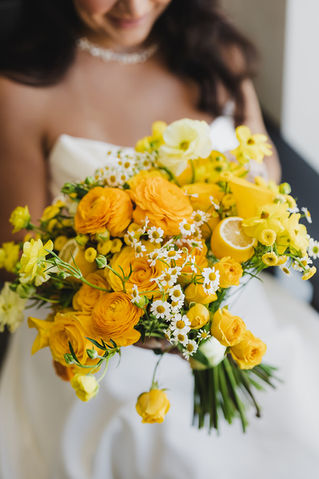 Bride holding vibrant yellow bouquet with ranunculus, chamomile, and lemon slices.