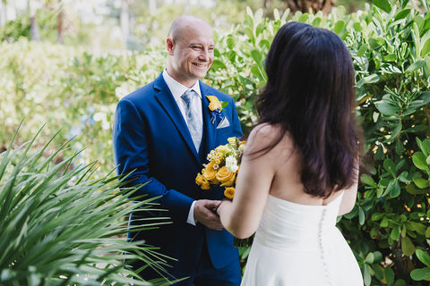 Groom smiles as he sees the bride for the first time during their first look, surrounded by tropical greenery.