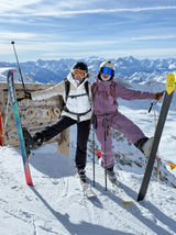 two skiers kick there legs out to pose for a photo with a snow covered mountain behind 