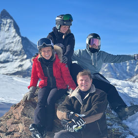 A family is posing for a photo on a rock in front of The Matterhorn in winter