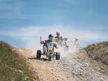 a group of people are flying down a dirt path on dirt scooters on a sunny summer day.