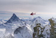 The iconic Air Zermatt helicopter flying over the snowy alpine scenery.
