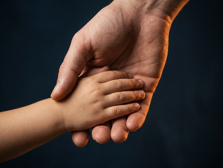 A small child's hand resting gently in the open palm of a larger adult hand, warmly lit against a deep midnight-blue background.