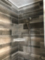 Tiled shower with gray wood-look tiles and shower head.
