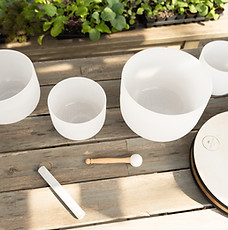 White crystal singing bowls and a mallet arranged on a wooden surface, ready for a community sound healing session outdoors.