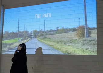 Andrea Joy Pearson speaking in front of a projected video during a live Journey of Becoming performance.