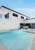 Modern Coastal Retreat – A stylish white luxury home with glass railings, contemporary design, and a bold black REEF sign against a blue sky. Private Outdoor Oasis – A pristine swimming pool surrounded by white stone landscaping, outdoor seating, and sleek modern architecture. Breathtaking Ocean Views – A scenic view of the coastline from the property, showcasing crashing waves, a coastal walking path, and lush greenery.