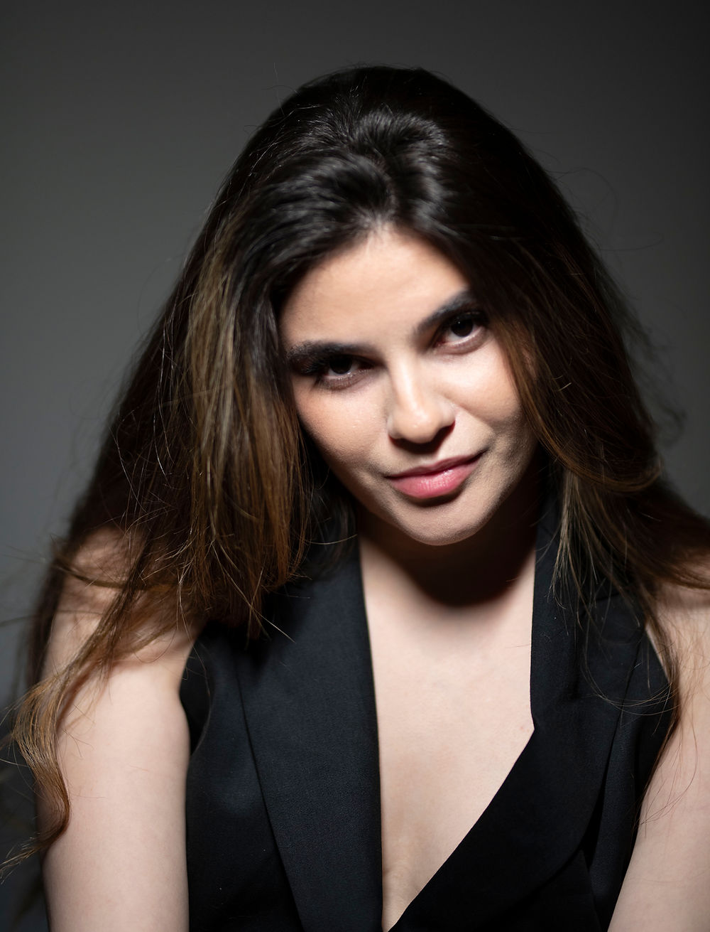 Young woman, long dark hair, black vest, with a soft gaze.