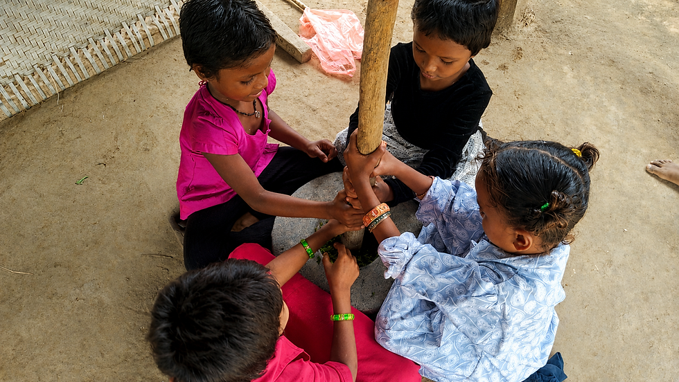 Children learning through participation as fresh Gorintaku leaves are prepared using a traditional grinding method.