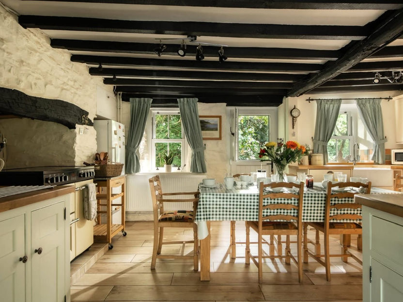 A traditional Swansea cottage kitchen with freshly painted black ceiling beams, white textured stone walls, and light sage green cabinets, professionally finished by Collins Painting and Decorating.