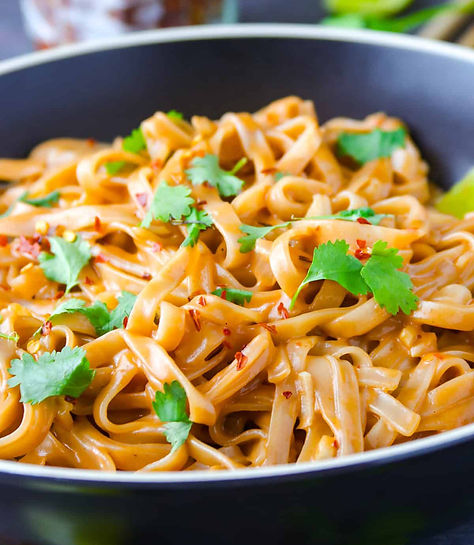 Eye-level view of a colorful plate of Pad Thai with noodles, bok choi, red bell pepper, and peanuts